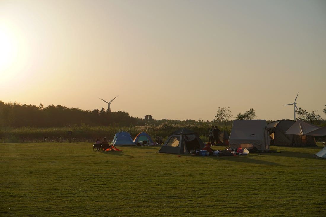 a group of people camping in a field with windmills in the background